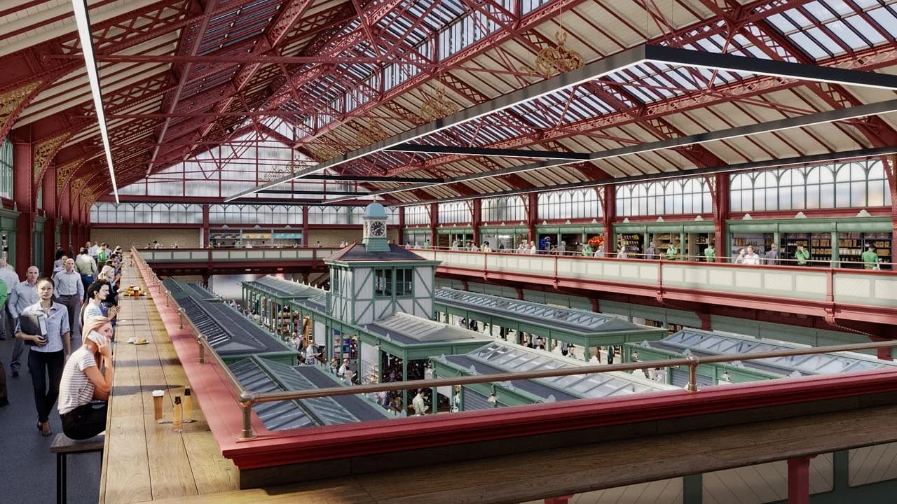 A bustling indoor market with a high, red-beamed ceiling and people milling about stalls and tables.